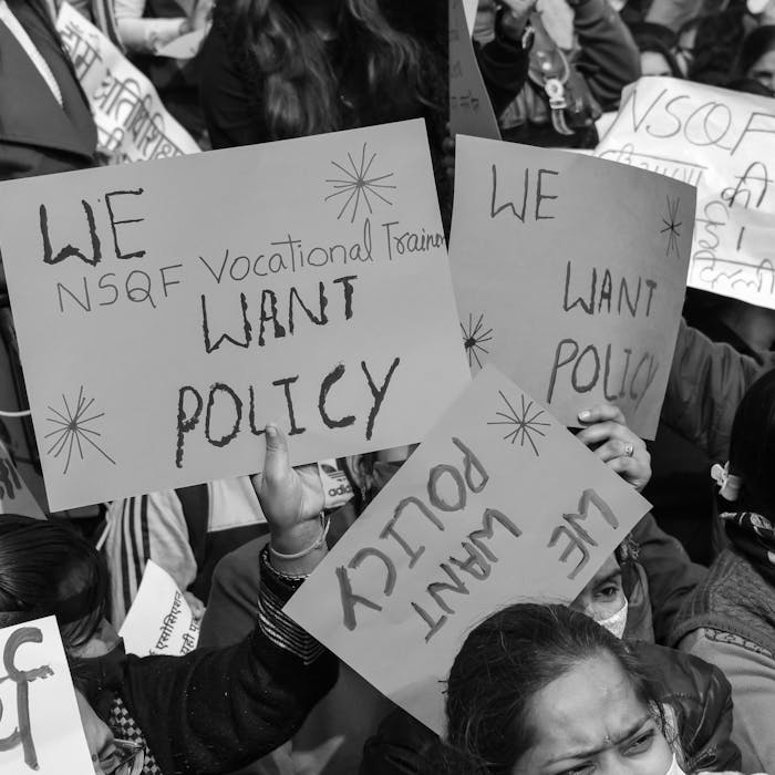 Black and white protest scene with participants holding signs demanding policy changes.